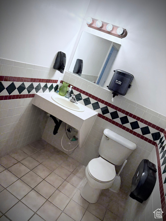 Bathroom with tile walls, a sink, toilet, and tile patterned floors