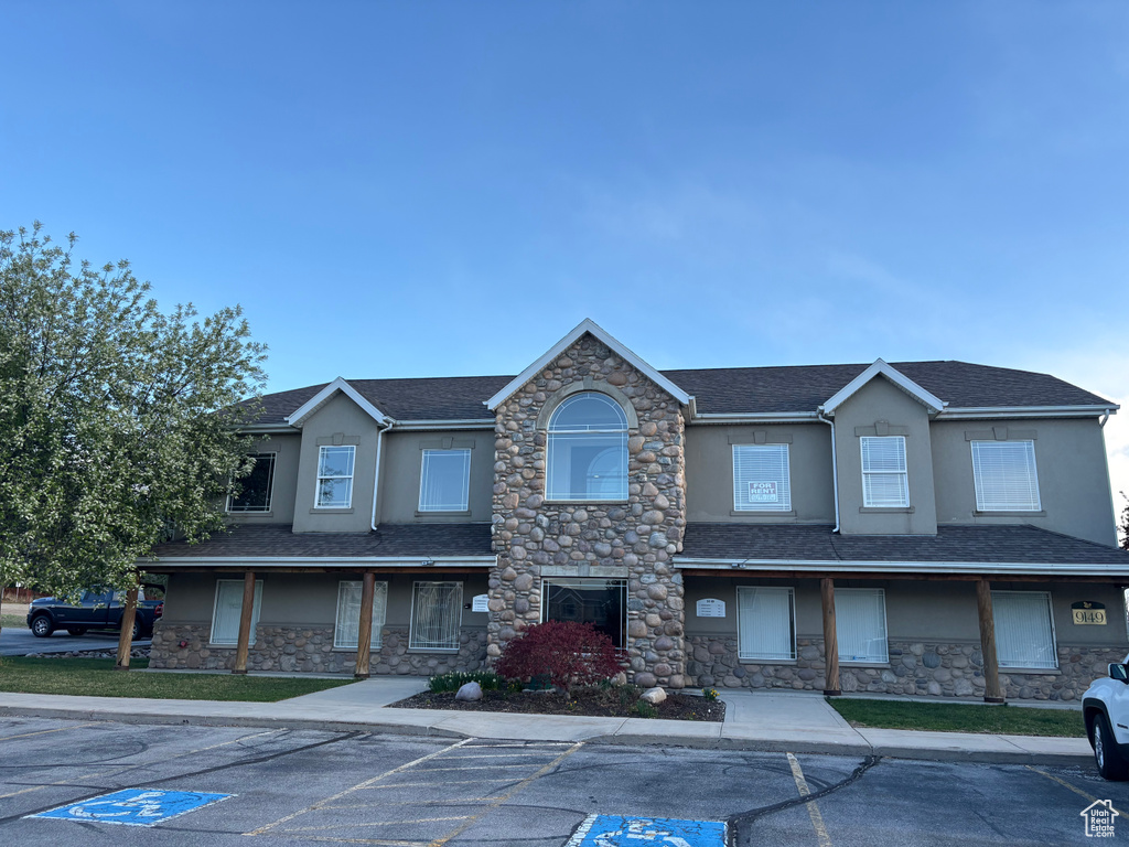 View of front facade featuring stucco siding, stone siding, uncovered parking, and a shingled roof