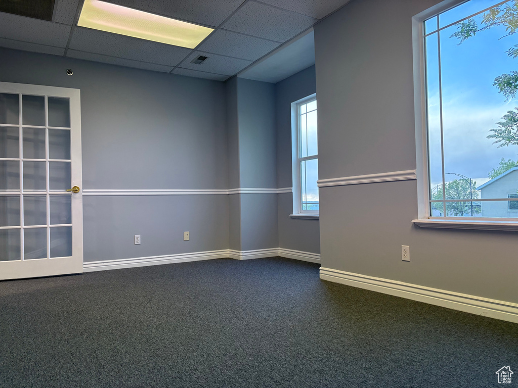 Unfurnished room with healthy amount of natural light, baseboards, dark colored carpet, and a paneled ceiling