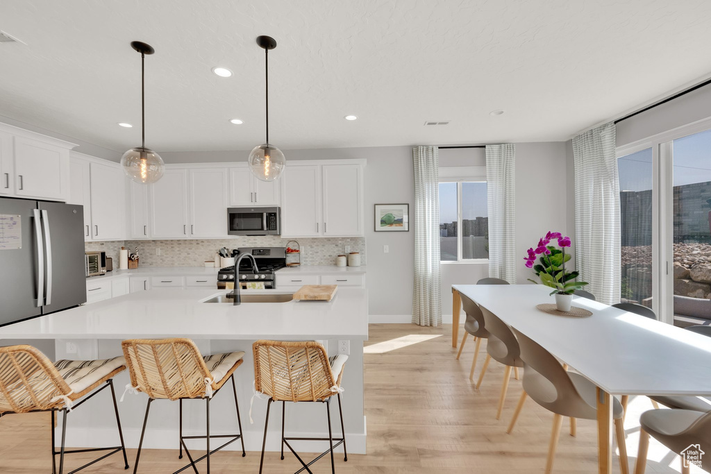 Kitchen with appliances with stainless steel finishes, backsplash, recessed lighting, a breakfast bar, and a kitchen island with sink