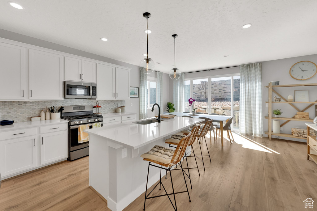 Kitchen featuring appliances with stainless steel finishes, a sink, light wood-type flooring, tasteful backsplash, and an island with sink