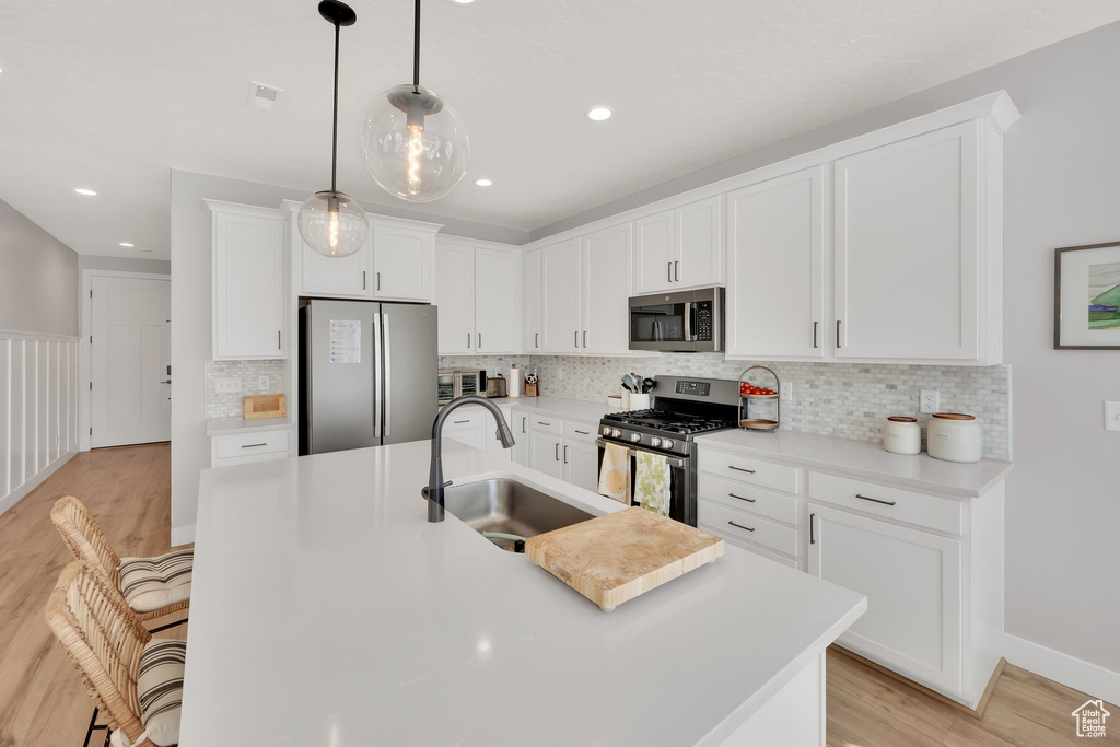 Kitchen featuring appliances with stainless steel finishes, a sink, light wood-style floors, a kitchen island with sink, and white cabinetry
