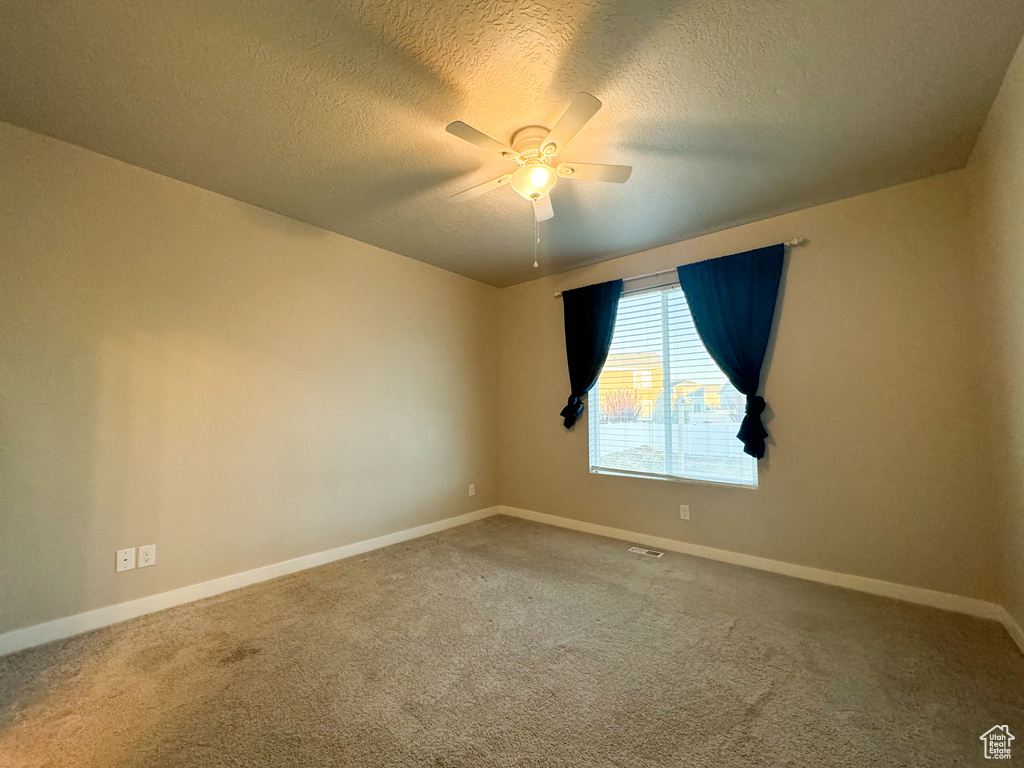 Carpeted empty room featuring a ceiling fan, baseboards, and a textured ceiling