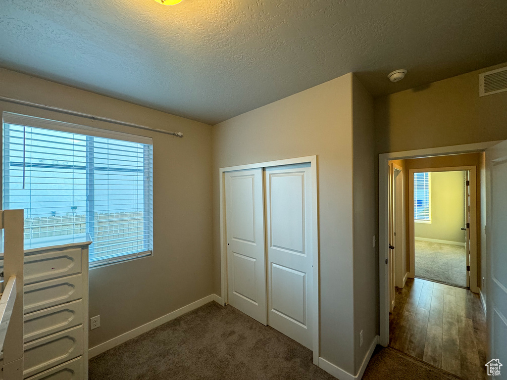 Unfurnished bedroom featuring a textured ceiling, a closet, baseboards, and carpet flooring