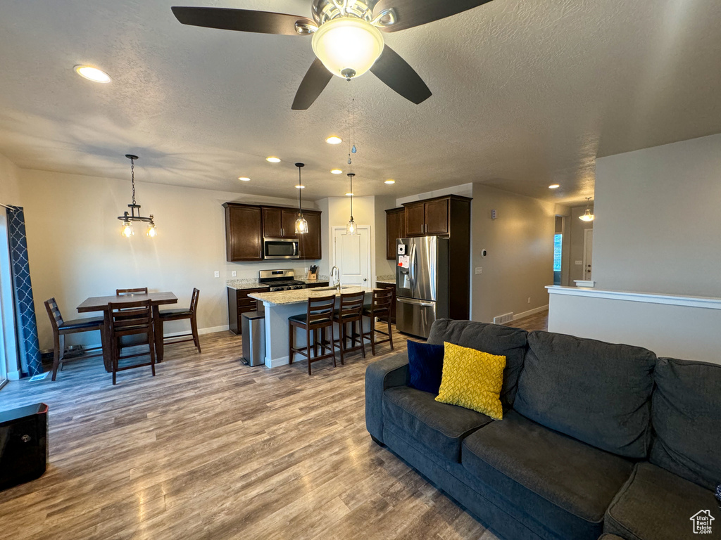 Living room featuring a textured ceiling, recessed lighting, wood finished floors, baseboards, and a ceiling fan