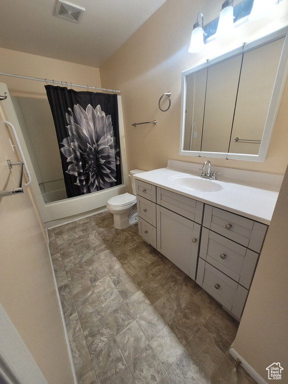 Bathroom with toilet, vanity, shower / tub combo, and stone finish floors