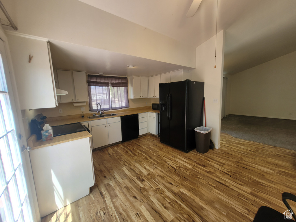 Kitchen featuring black appliances, a sink, light countertops, wood finished floors, and white cabinetry