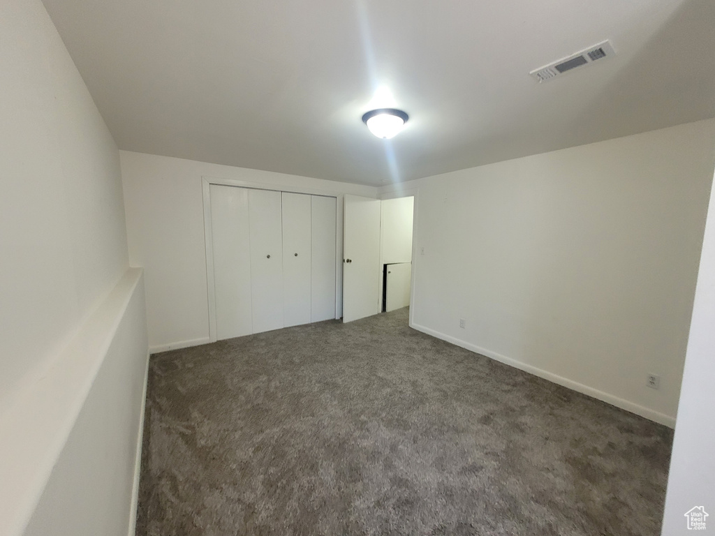Unfurnished bedroom featuring dark carpet, a closet, and baseboards