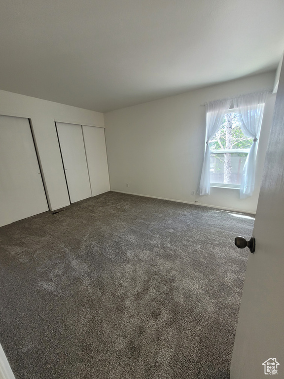 Unfurnished bedroom featuring dark colored carpet and multiple closets