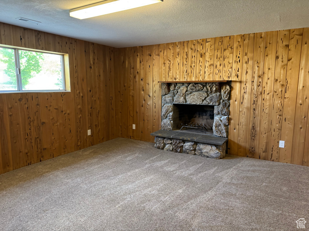 Unfurnished living room featuring carpet, a textured ceiling, a fireplace, and wood walls