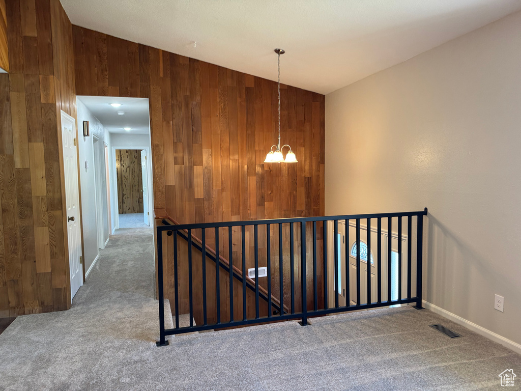 Stairs featuring a chandelier, carpet flooring, wooden walls, and baseboards