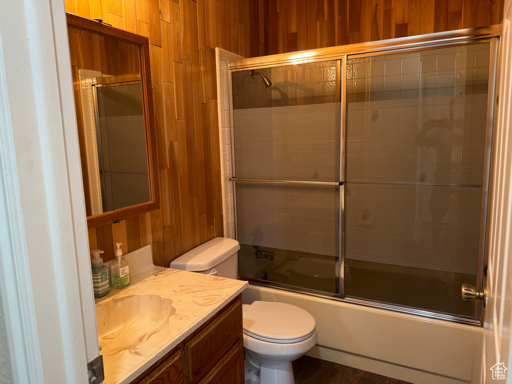 Bathroom featuring wood walls, toilet, bath / shower combo with glass door, and vanity