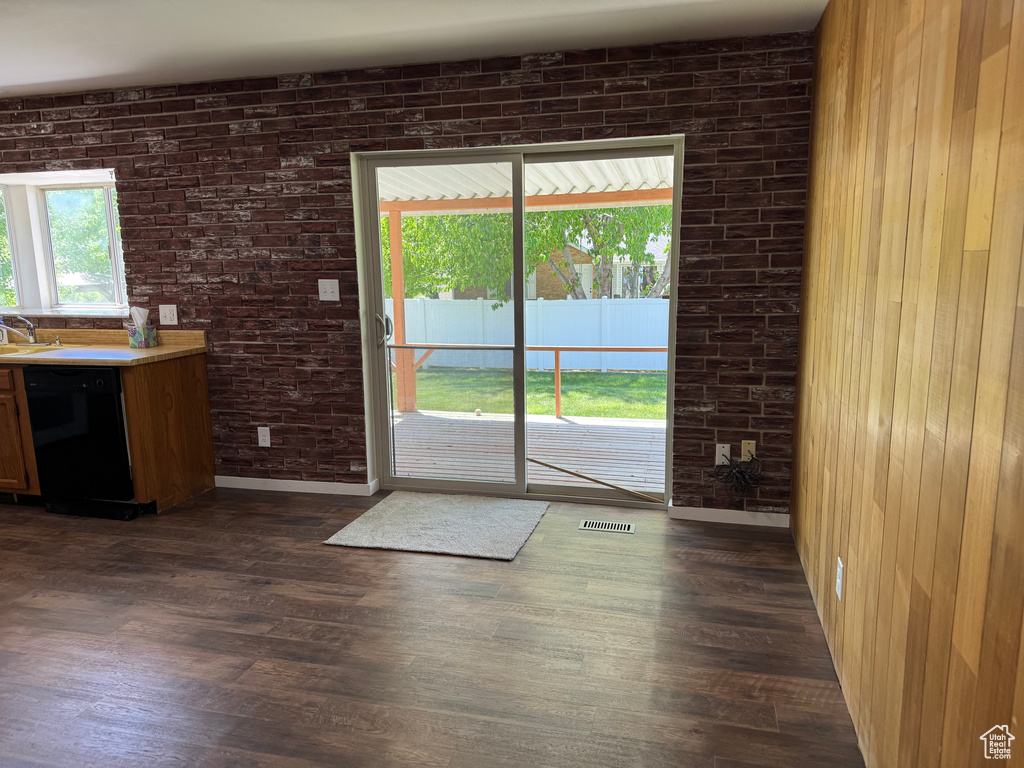Doorway featuring dark wood-style floors, a sink, brick wall, and wooden walls