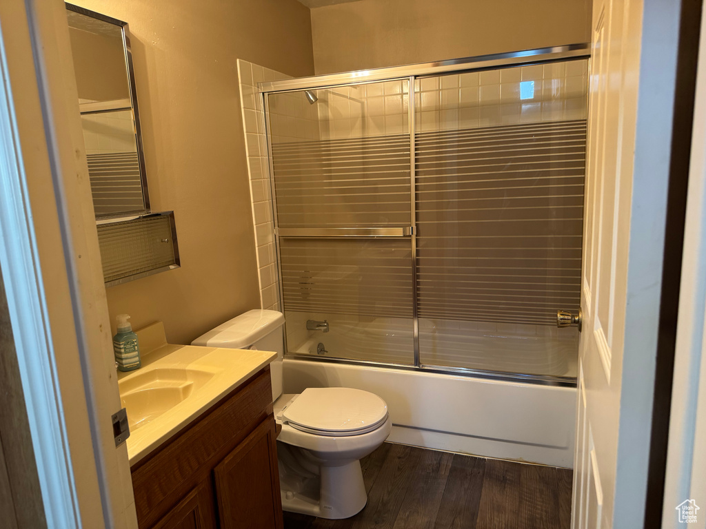 Bathroom with toilet, vanity, bath / shower combo with glass door, and wood finished floors