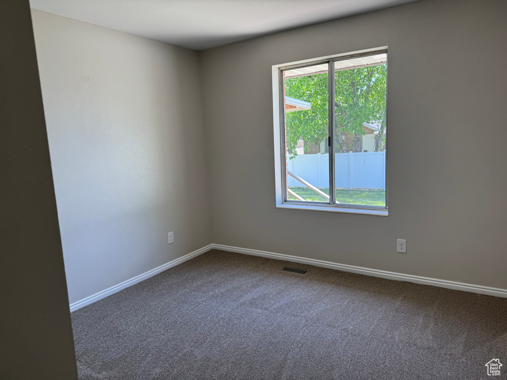Spare room featuring plenty of natural light, dark colored carpet, and baseboards