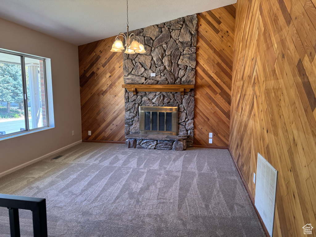 Unfurnished living room with baseboards, wood walls, a chandelier, a stone fireplace, and carpet flooring