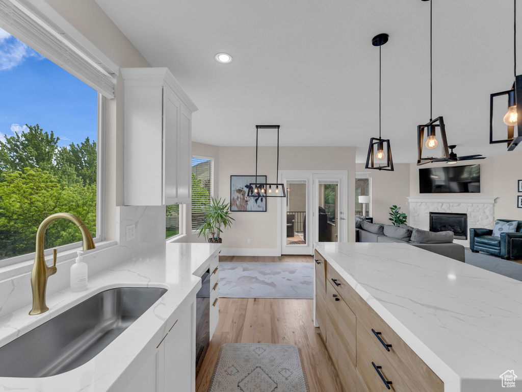 Kitchen featuring a sink, light wood-type flooring, light stone counters, a glass covered fireplace, and recessed lighting