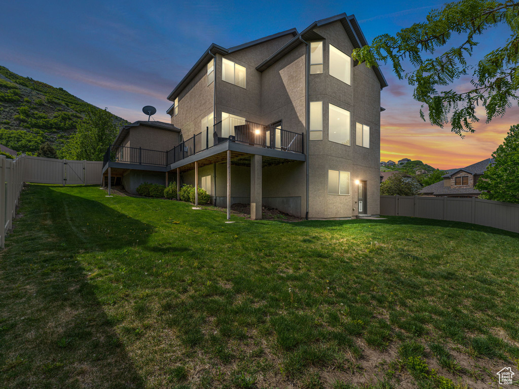 Back of property at dusk with a wooden deck, stucco siding, and a gate