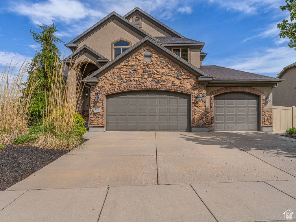 View of front facade with an attached garage, stone siding, driveway, and stucco siding