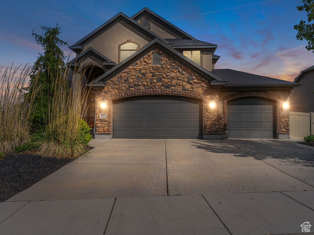 View of front facade with stone siding, an attached garage, concrete driveway, and stucco siding