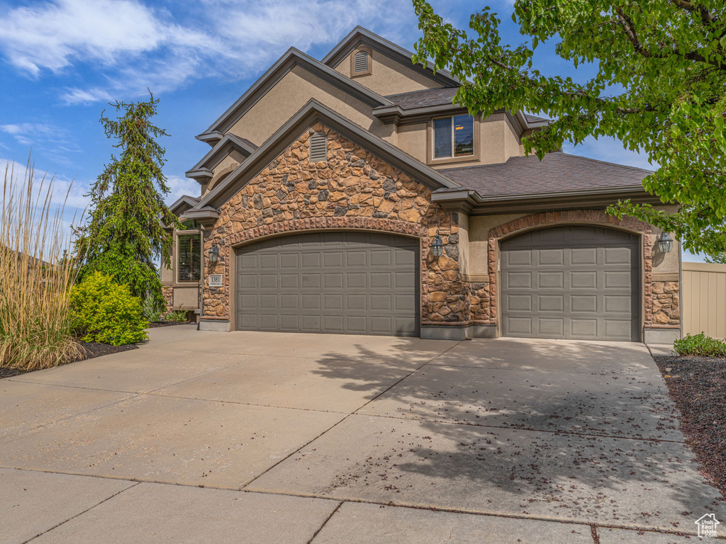 View of front of property with stone siding, a garage, driveway, and stucco siding