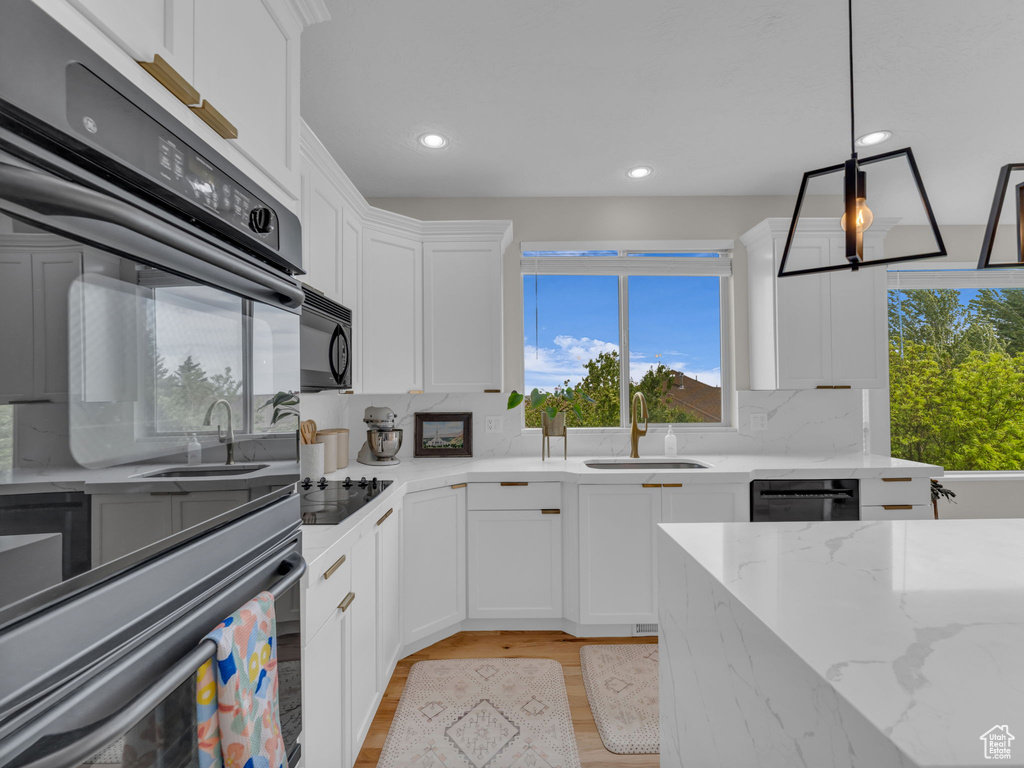 Kitchen with a sink, decorative backsplash, light wood-style flooring, black appliances, and white cabinets