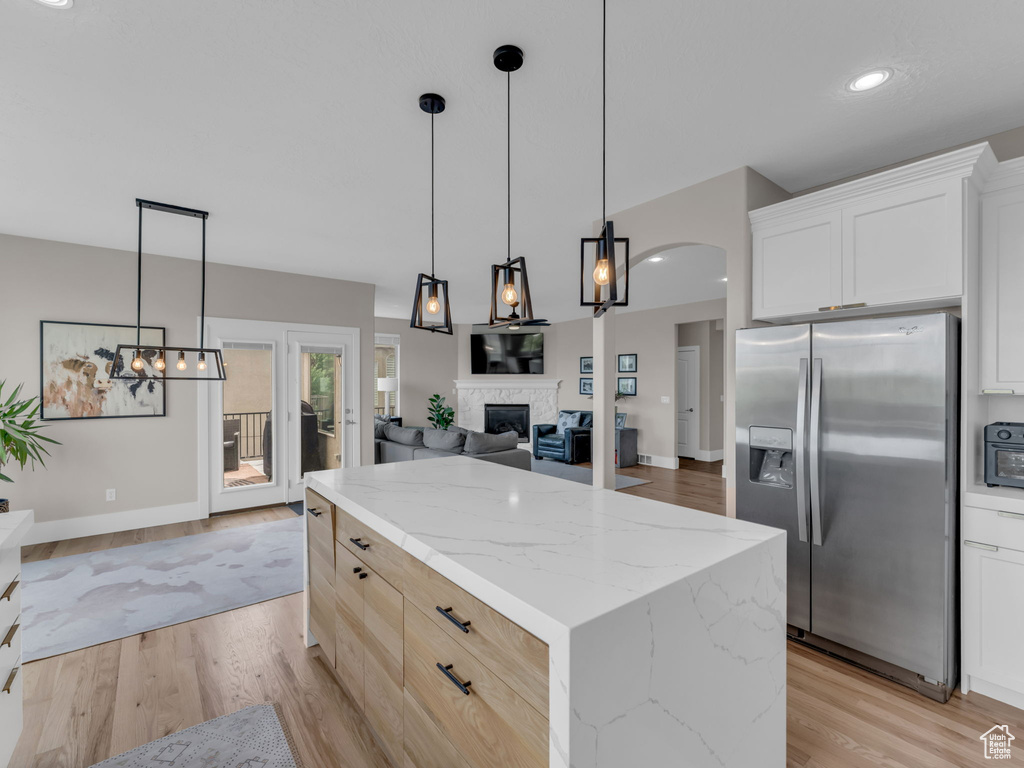 Kitchen with stainless steel fridge with ice dispenser, a center island, light wood-type flooring, a fireplace, and light stone counters