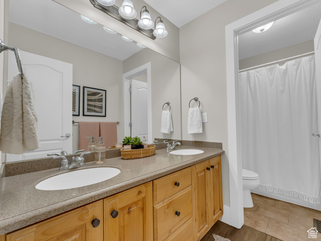 Bathroom with double vanity, toilet, curtained shower, and tile patterned floors