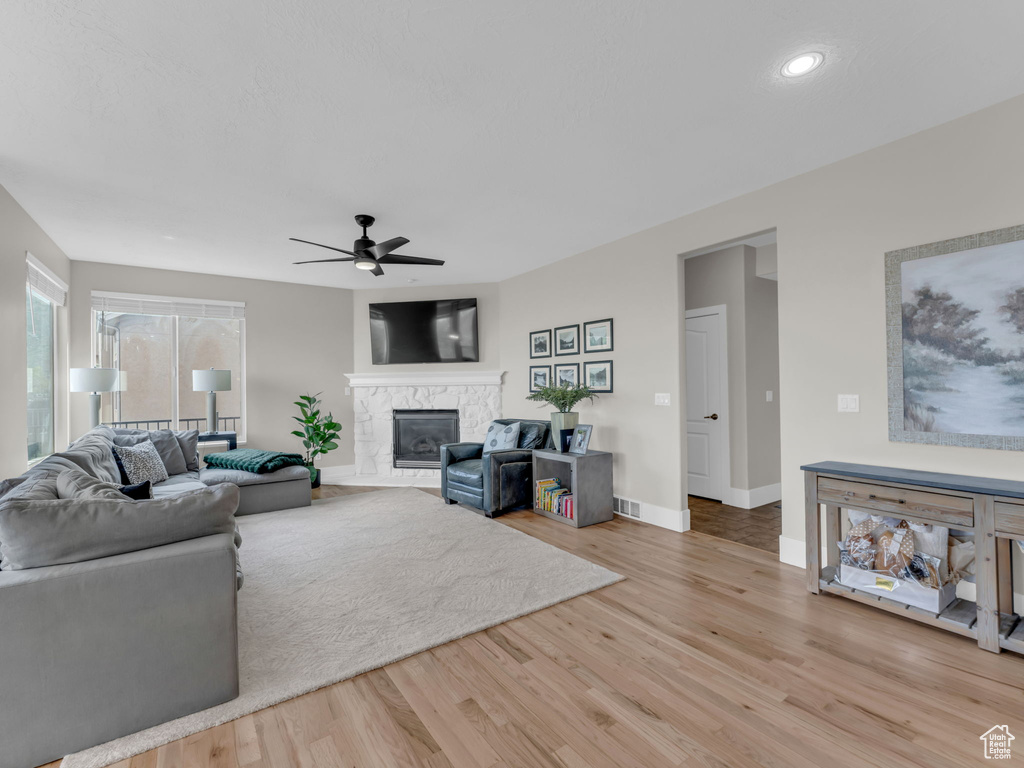 Living room with ceiling fan, light wood-style floors, a stone fireplace, baseboards, and recessed lighting
