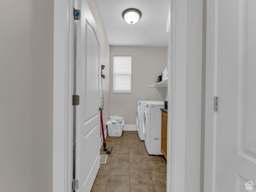 Clothes washing area featuring washer and clothes dryer, light tile patterned floors, and baseboards
