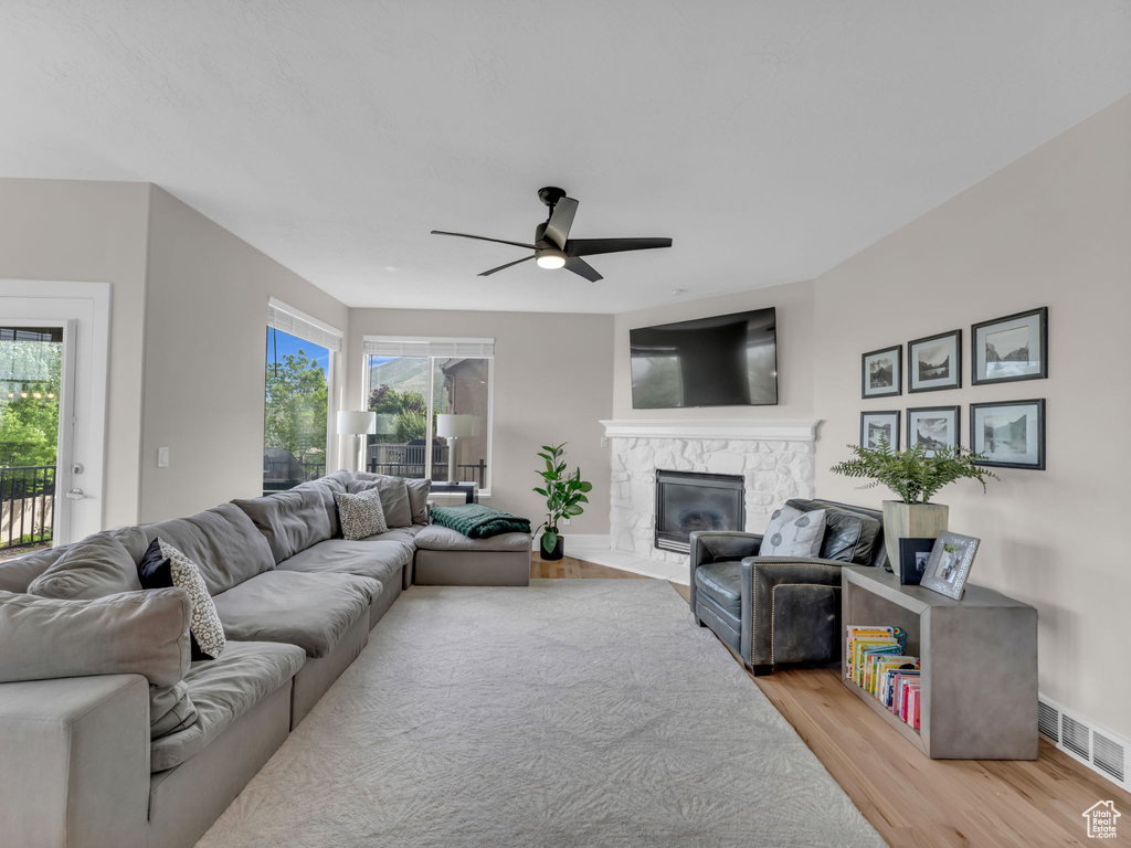 Living area with light wood-style flooring, ceiling fan, a fireplace, and plenty of natural light