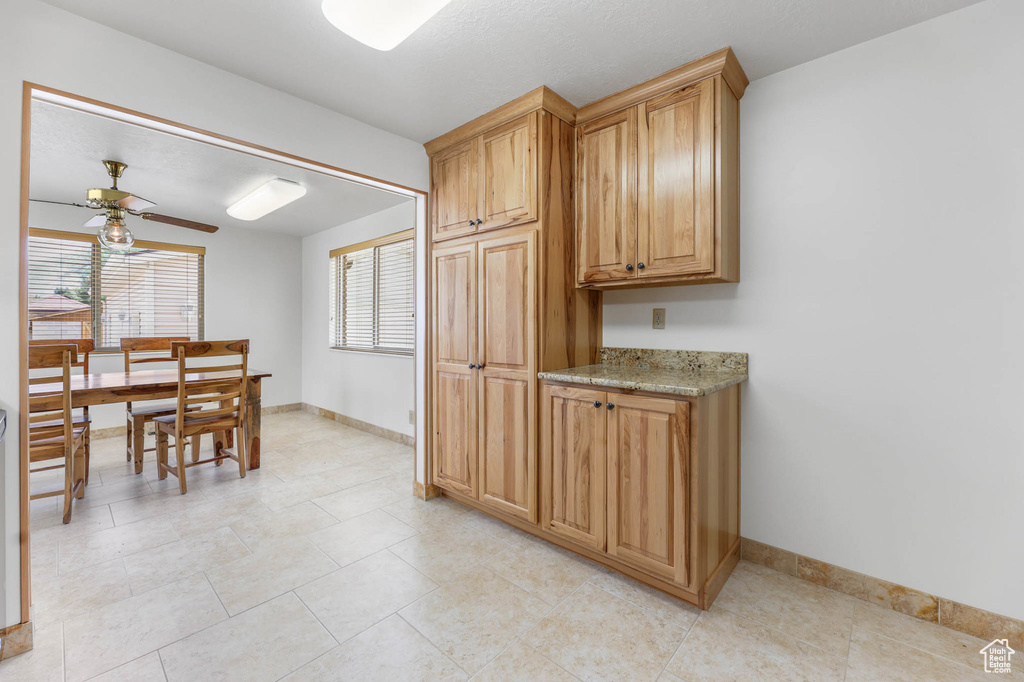 Kitchen with baseboards, a ceiling fan, light stone countertops, and light tile patterned floors