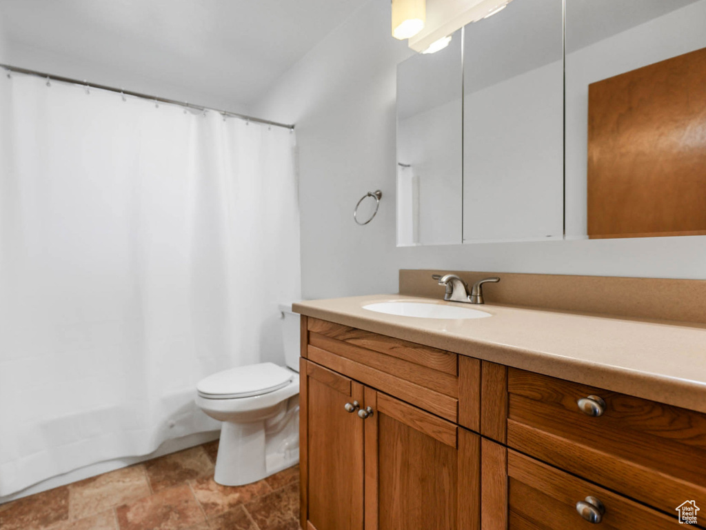 Full bathroom featuring toilet, vanity, stone finish flooring, and shower / bath combo