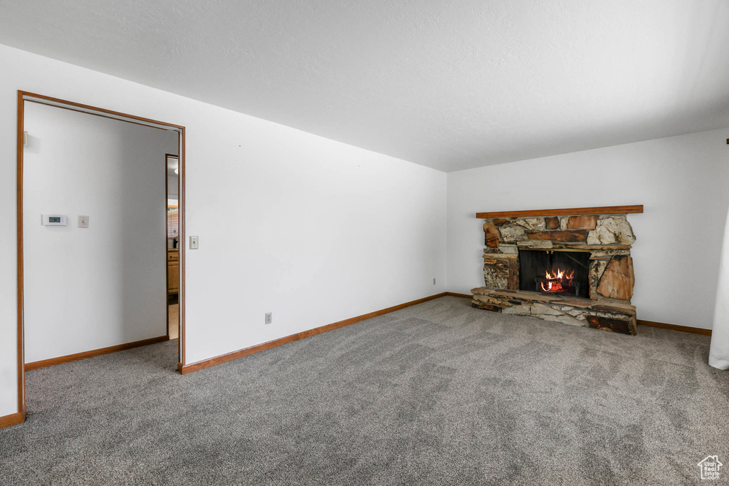 Unfurnished living room with carpet floors, a stone fireplace, and baseboards
