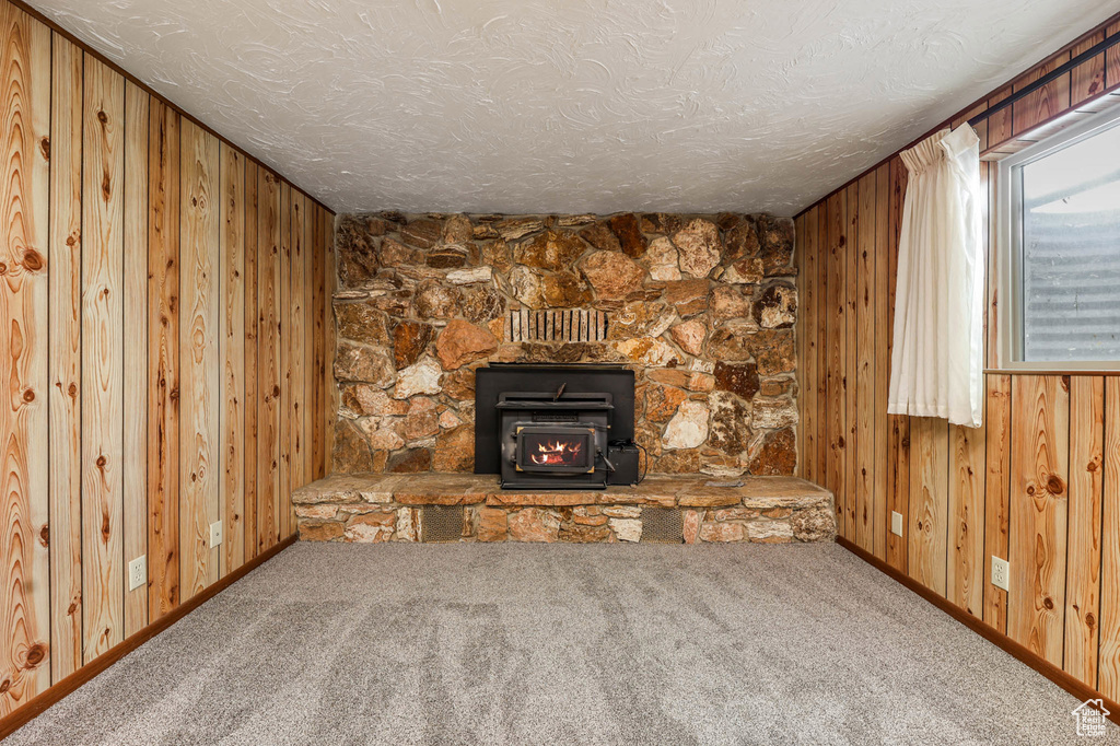 Unfurnished living room with wooden walls, carpet floors, a textured ceiling, a wood stove, and baseboards