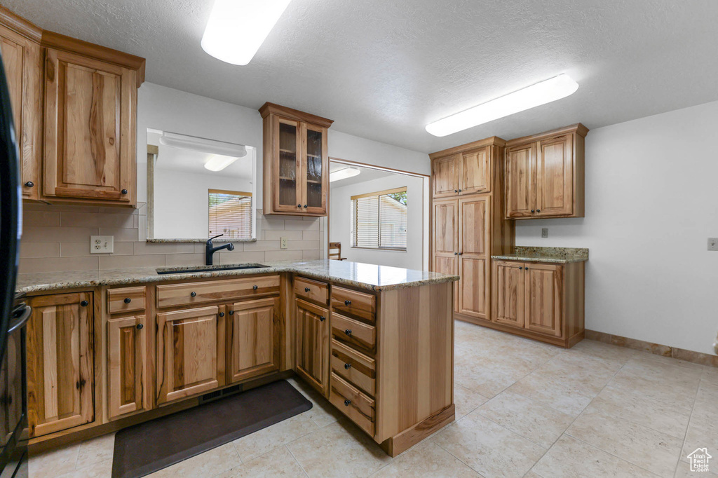 Kitchen with a sink, brown cabinets, a peninsula, glass insert cabinets, and tasteful backsplash