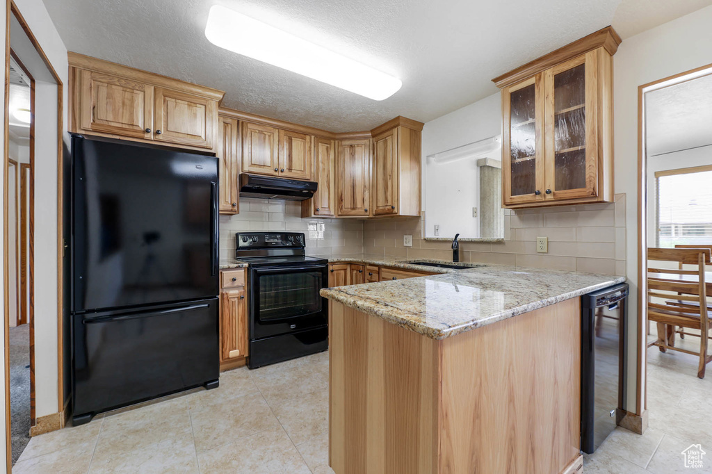 Kitchen featuring black appliances, under cabinet range hood, beverage cooler, light stone counters, and backsplash