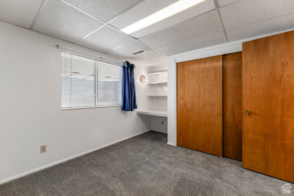 Unfurnished bedroom featuring carpet flooring, a paneled ceiling, a closet, and baseboards