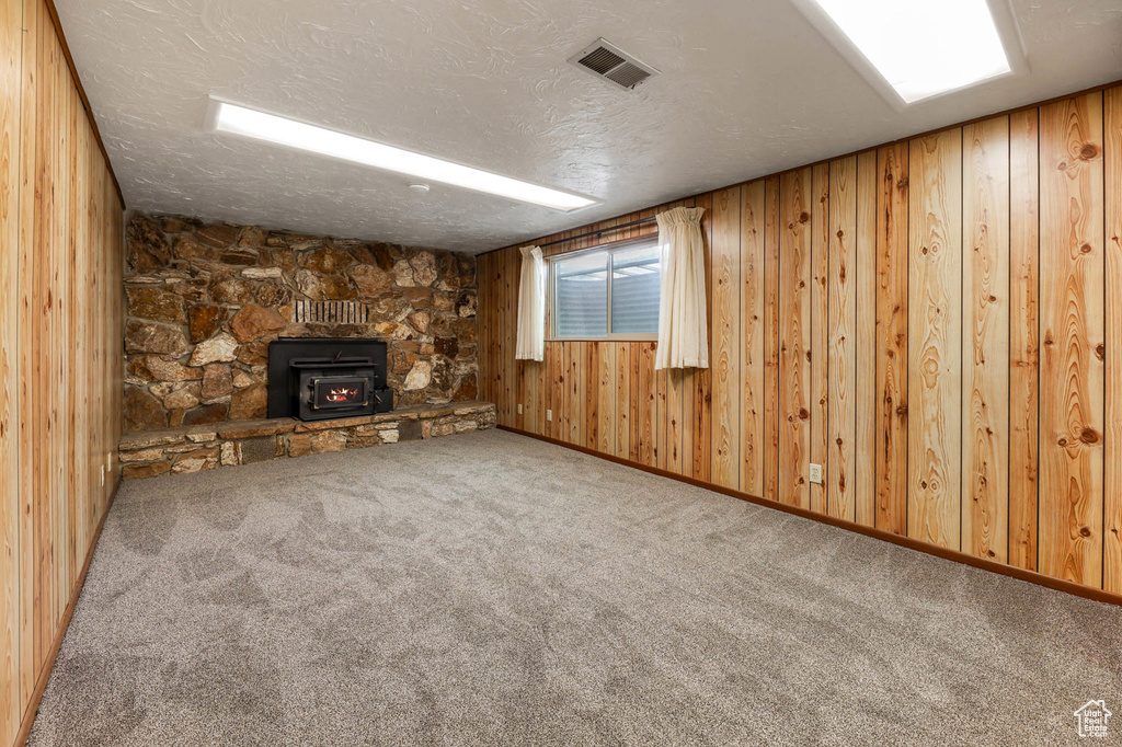 Unfurnished living room with carpet floors, a wood stove, wooden walls, and a textured ceiling