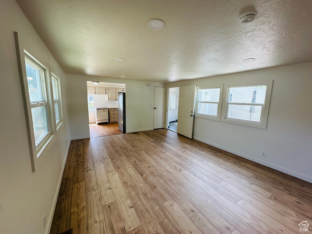 Unfurnished living room featuring baseboards, hardwood / wood-style flooring, and a textured ceiling