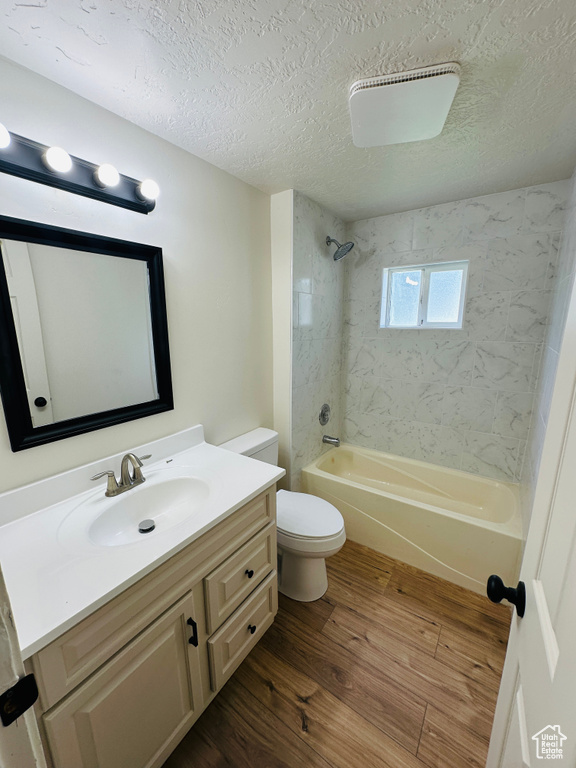 Bathroom with wood finished floors, shower / bathtub combination, vanity, a textured ceiling, and toilet
