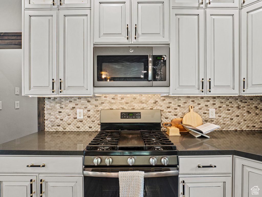Kitchen with appliances with stainless steel finishes, dark countertops, white cabinetry, and decorative backsplash