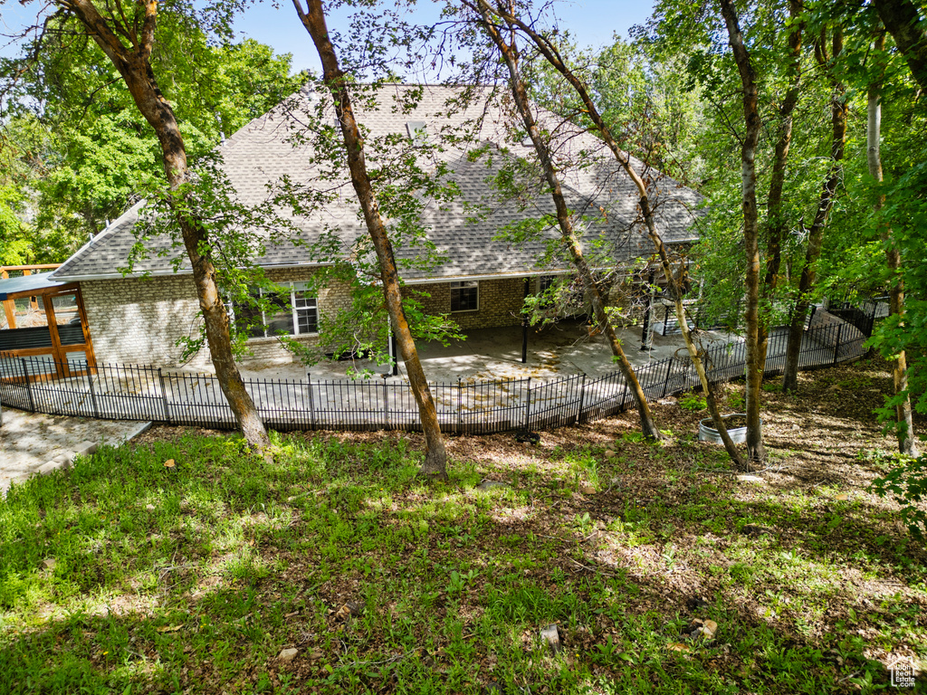 Back of house featuring a patio, brick siding, roof with shingles, and a fenced backyard