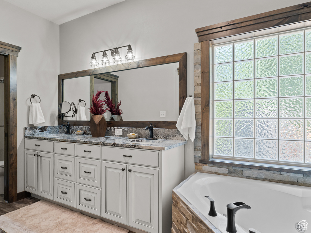 Full bathroom featuring a bath, double vanity, and wood finished floors