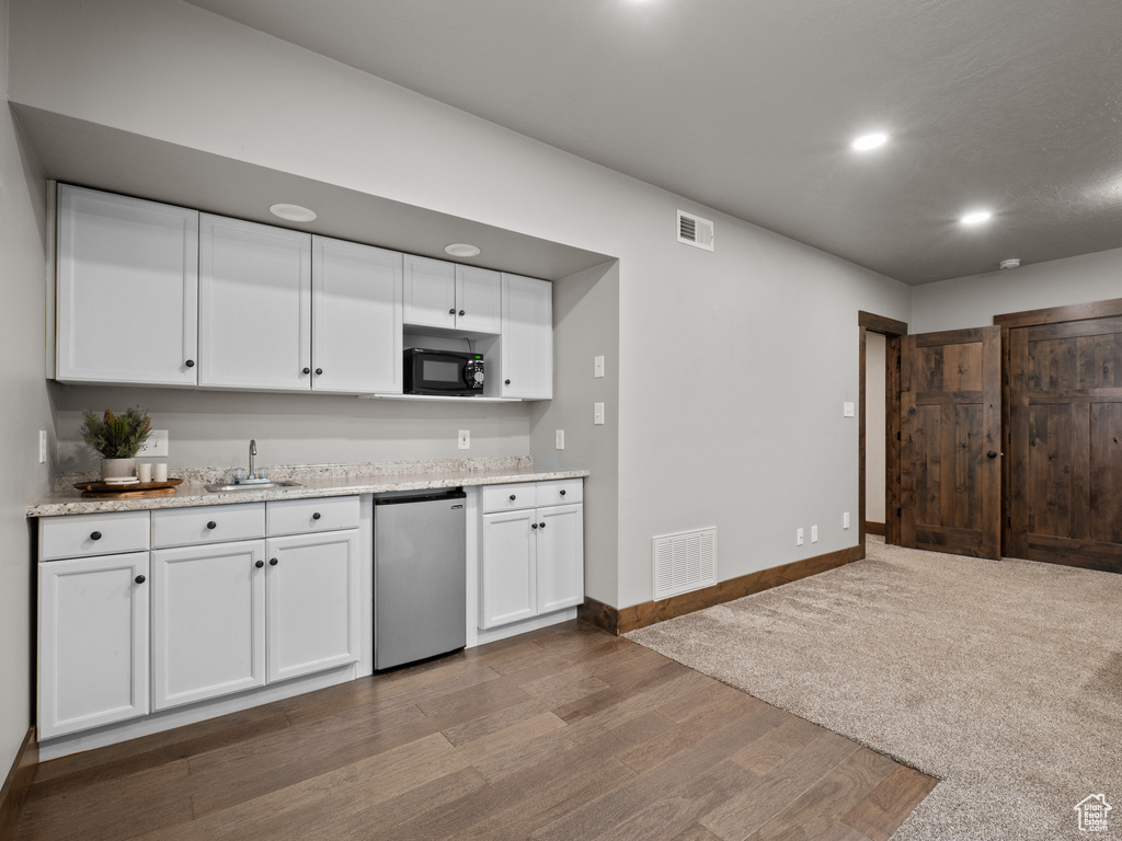 Kitchen with dishwashing machine, black microwave, white cabinetry, wood finished floors, and recessed lighting