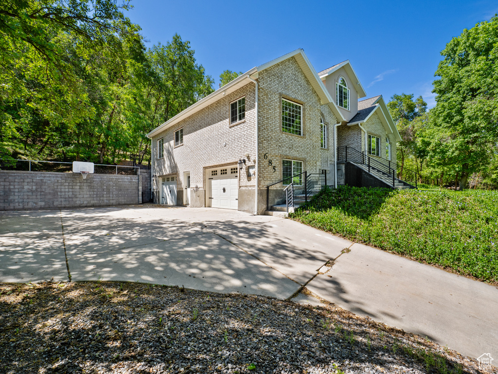 View of side of property with a garage, concrete driveway, brick siding, and fence
