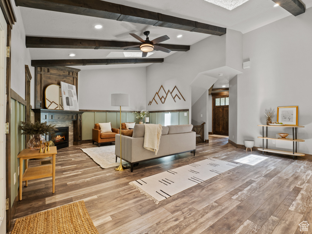 Living room featuring wood finished floors, ceiling fan, a fireplace, beamed ceiling, and recessed lighting