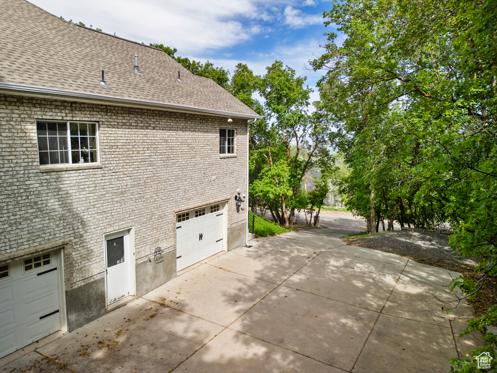 View of side of property with driveway, an attached garage, a shingled roof, and brick siding