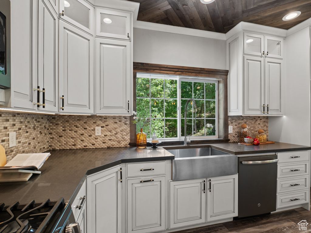 Kitchen with stainless steel dishwasher, dark countertops, a sink, wood ceiling, and white cabinets