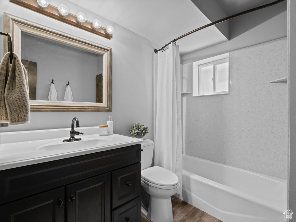 Bathroom with toilet, vanity, wood finished floors, and shower / bathtub combination with curtain